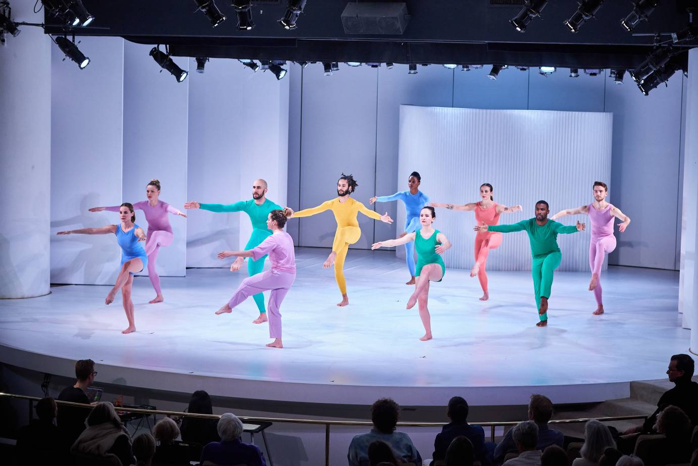 Dancers in bright unitards lift their leg forward in attitude as they contract